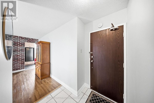 Apartment entryway with a dark wood door, wood flooring, and brick accent wall. - 1401 - 2130 Weston Road, Toronto