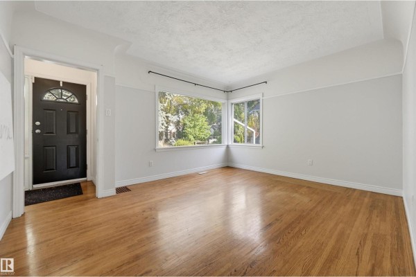 Living room with light grey walls, hardwood floors, and large corner windows. - 14019 106 Av Nw, Edmonton