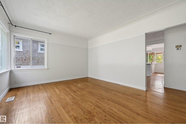 Living room with light grey walls, hardwood floors, and windows showing exterior view. - 14019 106 Av Nw, Edmonton