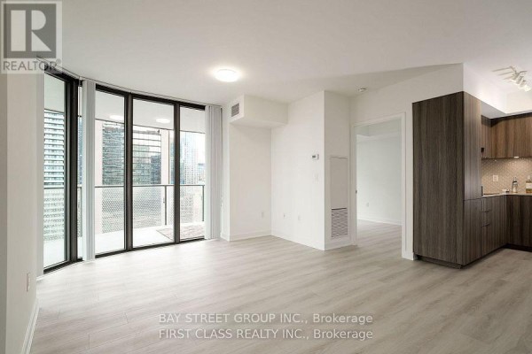 Living area with light wood floors and a view into a modern kitchen with dark wood cabinetry. - 1402 - 11 Wellesley Street W, Toronto