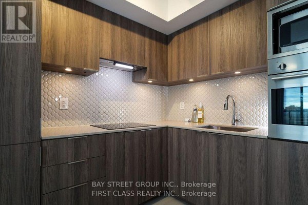Corner kitchen with dark wood cabinets, light tiled backsplash, stainless steel appliances, and quartz counters. - 1402 - 11 Wellesley Street W, Toronto