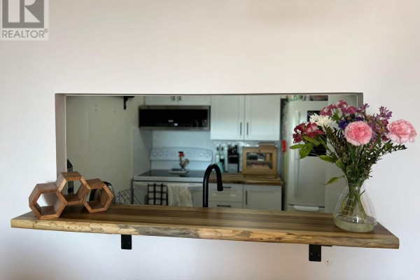 Wooden shelf with decorative items and a vase of flowers overlooking a kitchen area. - #1402 - 3 Hickory Tree Road, Toronto
