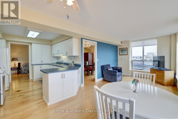 Living room with dining area, kitchen, blue armchair, and large window - 1402 - 442 Maple Avenue Burlington
