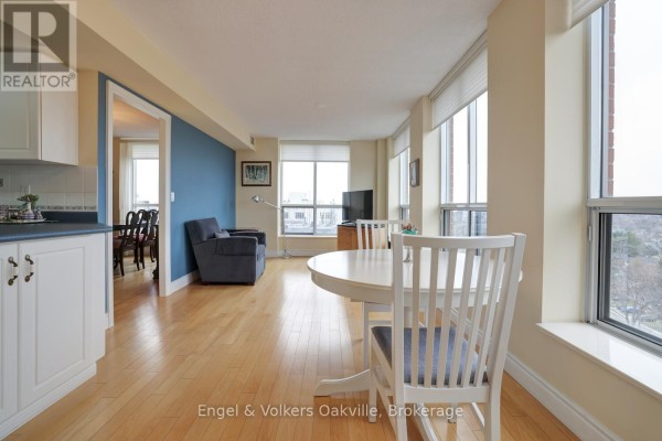 Living room with dining table, chairs, armchair, TV, and large windows - 1402 - 442 Maple Avenue Burlington