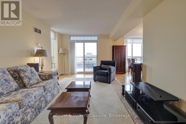 Living room with floral sofa, armchair, coffee tables, and balcony access - 1402 - 442 Maple Avenue Burlington