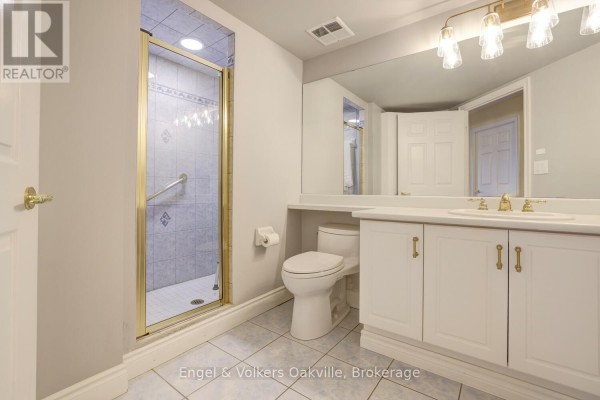 Bathroom with glass shower, white vanity, dual sinks, and toilet - 1402 - 442 Maple Avenue Burlington