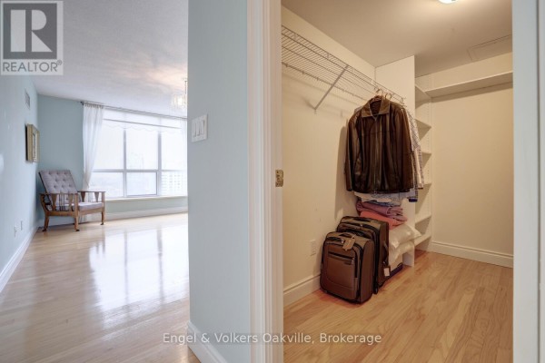 Walk-in closet with luggage and clothes, adjacent to a living area with armchair and large window - 1402 - 442 Maple Avenue Burlington
