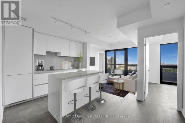 Open concept kitchen with white cabinetry, island with bar stools, and living area. - 1403 - 4015 The Exchange, Mississauga