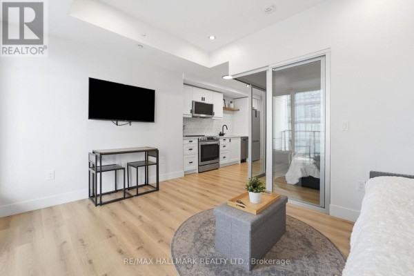 Open concept studio apartment showing the living area, a compact kitchen with white cabinetry, and glass doors to a bedroom. - 1403 - 5 Wellington Street S, Kitchener