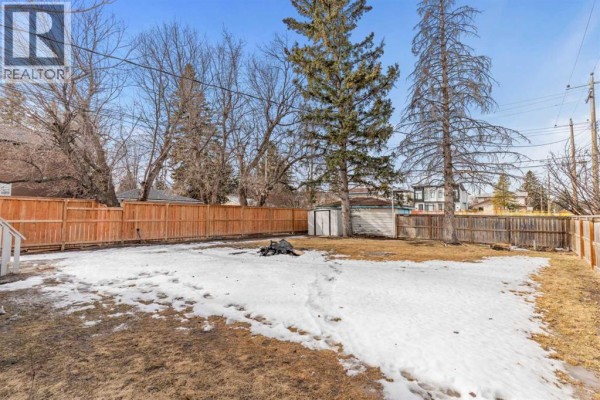 Spacious backyard with snow, trees, and a fire pit area. - 1403 43 Street Sw, Calgary