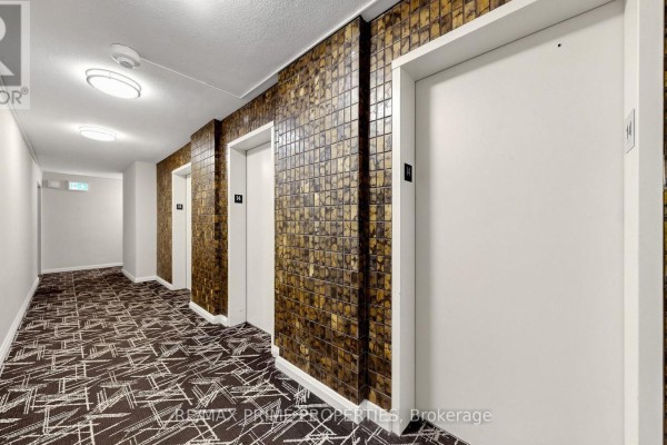 Apartment building hallway with beige patterned carpet, textured wall, and three elevators. - 1404 - 1455 Lawrence Avenue W, Toronto