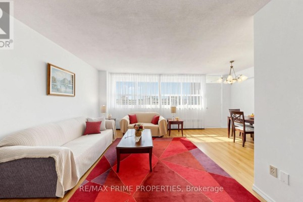 Living room with two sofas, a red geometric rug, and a large window with white curtains. - 1404 - 1455 Lawrence Avenue W, Toronto