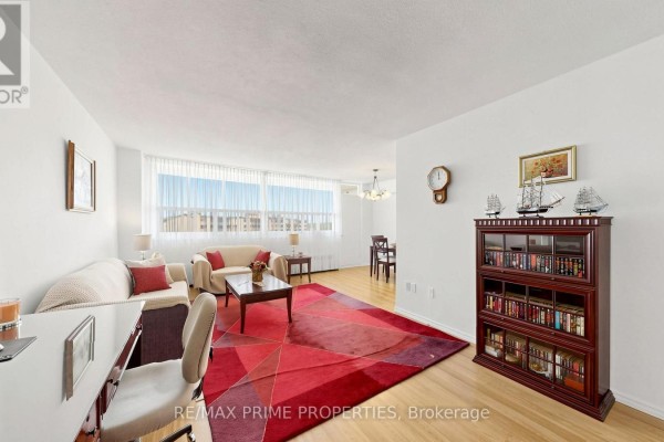 Living and dining area with wooden floors, a sofa, red rug, and a dark wood bookcase. - 1404 - 1455 Lawrence Avenue W, Toronto