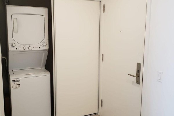 Stacked white washer and dryer unit next to a white door with a silver handle. - 1404 - 33 Helendale Avenue, Toronto