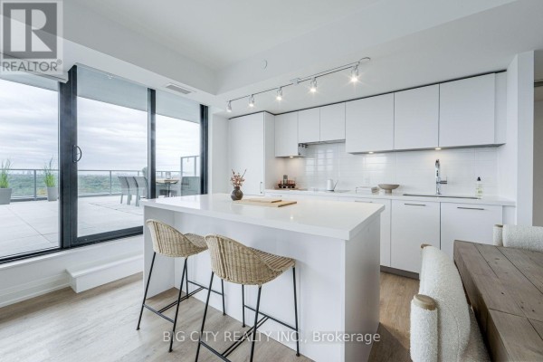Modern white kitchen with a large island, pendant lights, and white subway tile backsplash. - 1404 - 36 Brentcliffe Road, Toronto