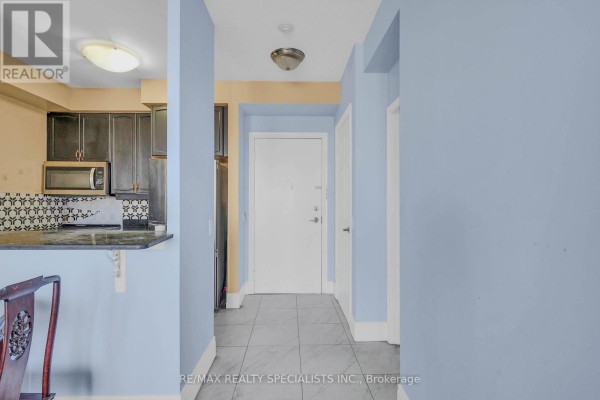 Apartment entryway with light blue walls, dark kitchen cabinets, and a white door. - 1404 - 710 Humberwood Boulevard, Toronto