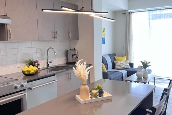 Kitchen island with decorative items, grey cabinets, and stainless steel sink. - 1404 - 8960 Jane Street E, Vaughan