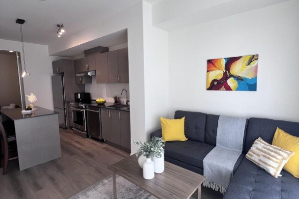 Living area with grey sectional sofa, yellow pillows, and artwork on wall. - 1404 - 8960 Jane Street E, Vaughan