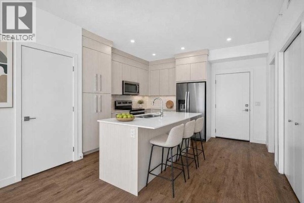 Corner kitchen with light wood cabinetry, an island with bar stools, and stainless steel appliances. - 1405, 681 Savanna Boulevard Ne, Calgary