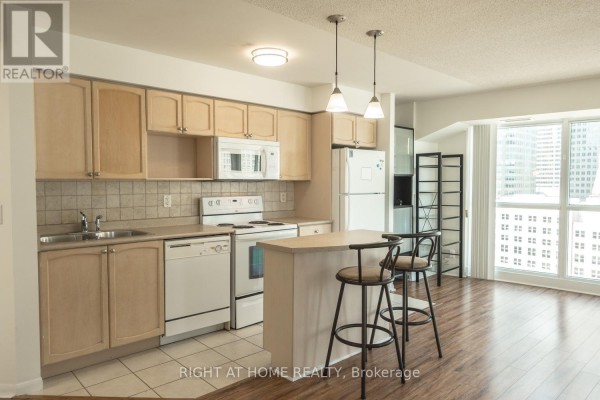 Kitchen area with light wood cabinets, white appliances, tile backsplash, and island with bar stools. - 1405 - 18 Yonge Street, Toronto