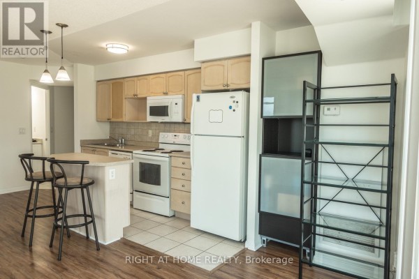 Kitchen area with light wood cabinets, white appliances, tile backsplash, island, and shelving unit. - 1405 - 18 Yonge Street, Toronto