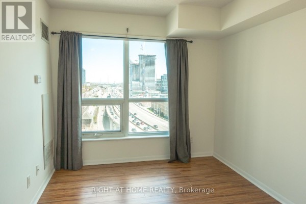 Bedroom with large window overlooking city skyline and traffic, featuring grey curtains and hardwood floors. - 1405 - 18 Yonge Street, Toronto