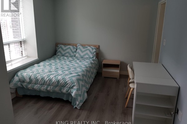 Bedroom with a queen-size bed, light blue walls, a nightstand, and a white desk with a chair. - 1405 - 318 Spruce Street, Waterloo