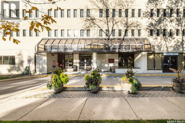 Entrance to the apartment building with a glass awning, planters, and brick facade. - 1405 315 5th Avenue N, Saskatoon
