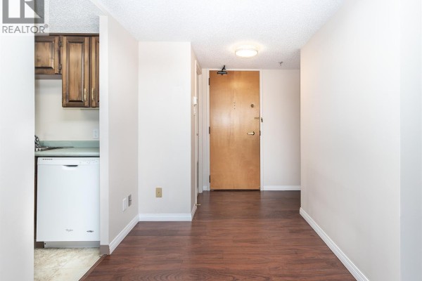 Hallway entrance to an apartment with dark wood floors, light walls, and a wooden door. - 1405 315 5th Avenue N, Saskatoon