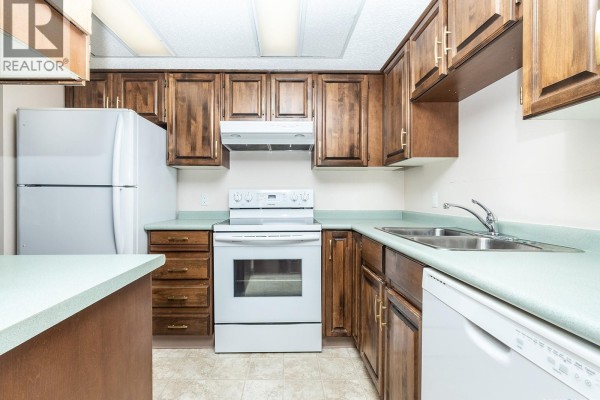 Kitchen with dark wood cabinets, white appliances, a stove, sink, and light green countertops. - 1405 315 5th Avenue N, Saskatoon