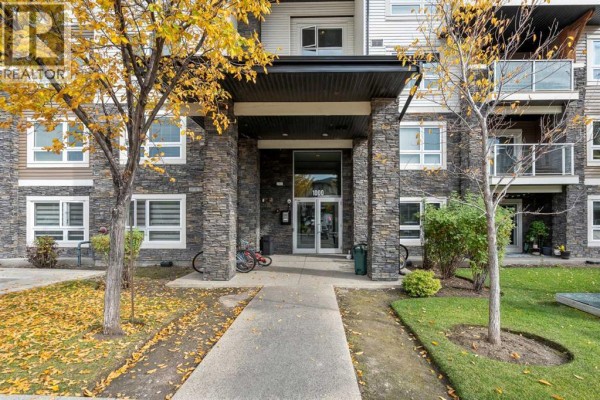 Entrance to an apartment building with a covered walkway, stone facade, and trees. - 1406, 240 Skyview Ranch Road Ne, Calgary