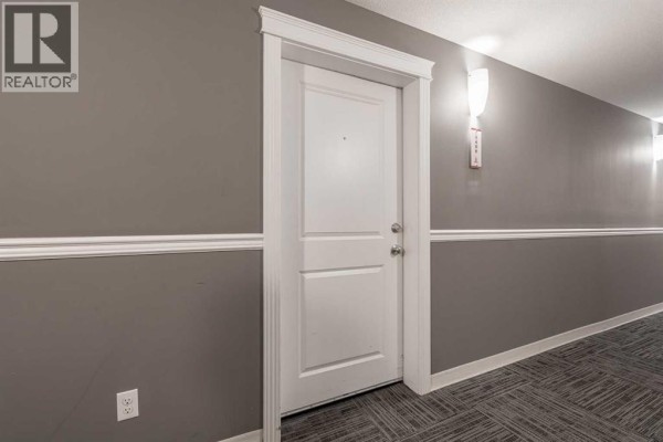 Interior apartment hallway with a white door, grey walls, and patterned carpet. - 1406, 240 Skyview Ranch Road Ne, Calgary