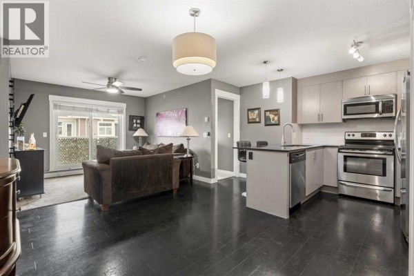Open concept living area and kitchen with dark floors, a sofa, and stainless steel appliances. - 1406, 240 Skyview Ranch Road Ne, Calgary