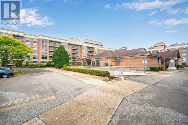 Exterior view of a brick apartment building with balconies and a covered entrance on a sunny day. - 1406 - 100 Burloak Drive, Burlington