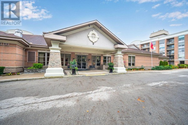 Front entrance of the apartment building with brick facade, stone columns, and a beige roof. - 1406 - 100 Burloak Drive, Burlington