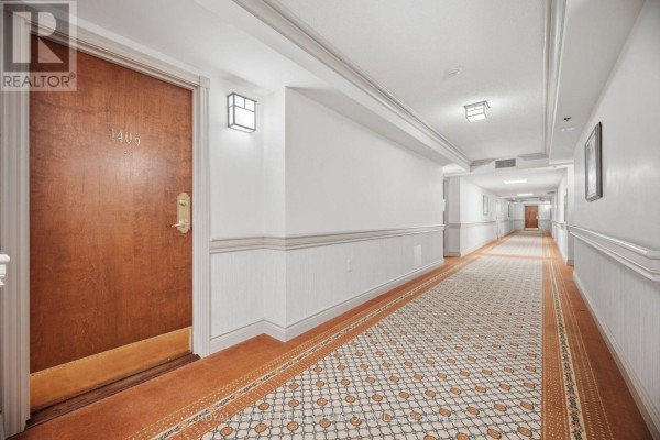 Apartment building hallway with wood doors, beige and orange patterned carpet, and white wainscoting. - 1406 - 100 Burloak Drive, Burlington