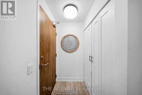 Apartment entryway with a wood door, white closet doors, and decorative wall art. - 1406 - 1215 Bayly Street, Pickering