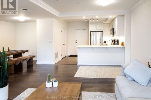 Living and dining area with dark wood floors, a sofa, dining table, and view of the kitchen. - 1406 - 505 Talbot Street, London East