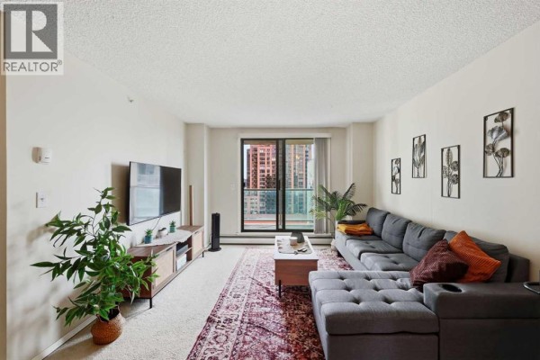 Expansive view of the living area, showcasing a sectional sofa and city skyline through the window. - 1407, 1111 6 Avenue Sw, Calgary