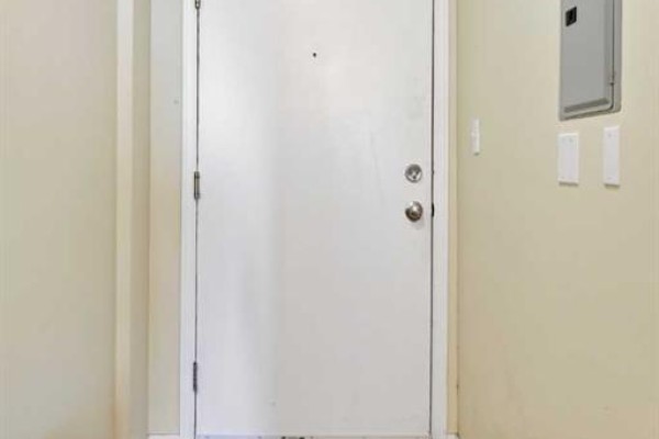 A closed white apartment door with silver knob and a grey electrical panel on the wall. - 1407, 1111 6 Avenue Sw, Calgary