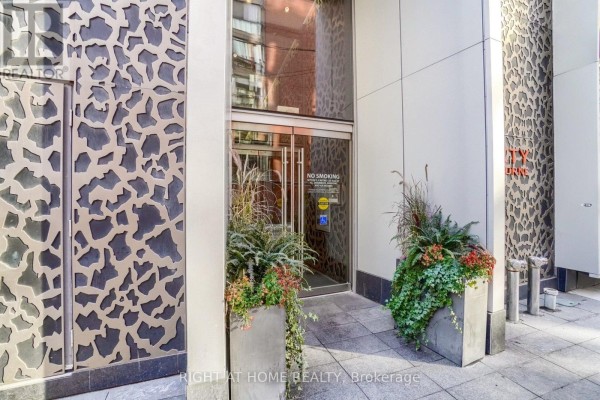 Building entrance with glass doors, planters with foliage, and textured metal wall panels. - 1407 - 60 Colborne Street, Toronto