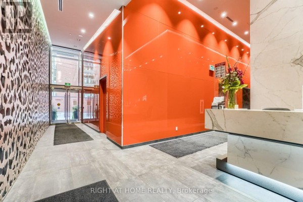 Building lobby with orange glass walls, a marble reception desk, and decorative lighting. - 1407 - 60 Colborne Street, Toronto