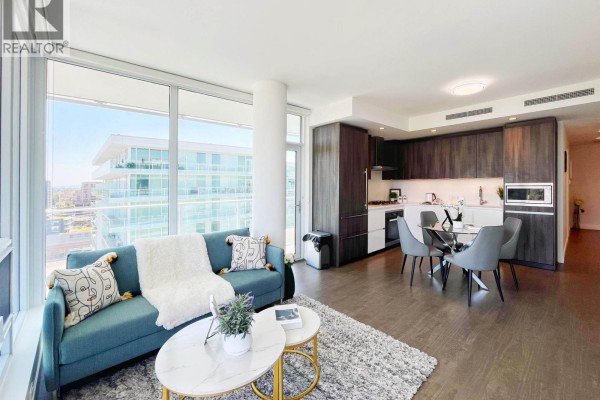Open-concept living and kitchen area with a teal sofa, dining table, and dark wood cabinets. - 1407 6328 No. 3 Road, Richmond