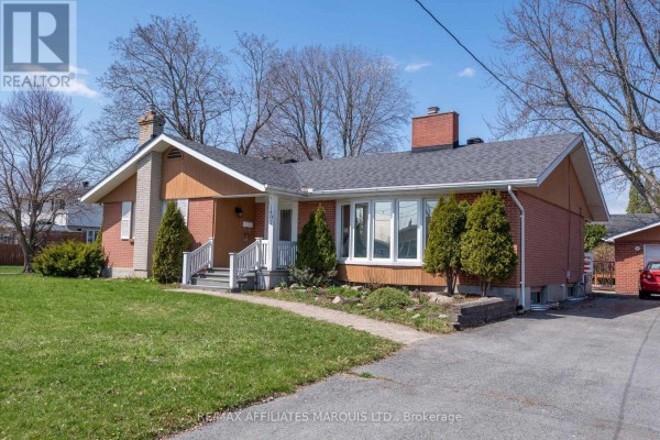 Side view of a red brick bungalow with a driveway, garage, and green lawn. - 1407 Boyd Street S, Cornwall