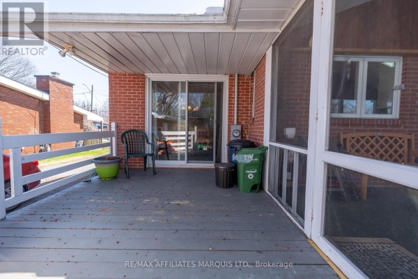Screened-in porch with a sliding glass door, chairs, and trash bins. - 1407 Boyd Street S, Cornwall
