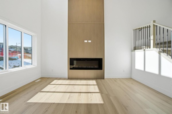 Spacious living room with white walls, large windows, light wood floors, and a floor-to-ceiling wood slat accent wall with a fireplace. - 1407 Osprey Co Nw, Edmonton