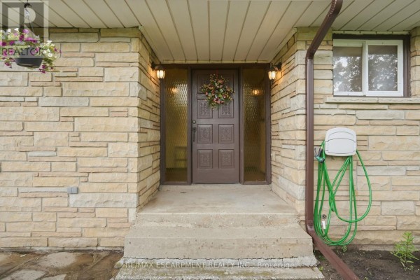 Close-up of the front entrance with a brown door, glass sidelights, and stone facade. - 1408 Edgewood Road, Hamilton
