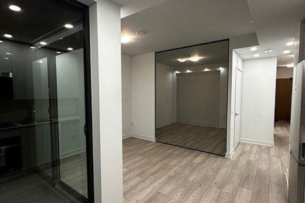 View of the open-concept living area with light wood flooring, white walls, and a mirrored closet door. - 1409 - 2920 Hwy 7, Vaughan