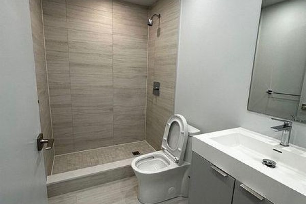 A minimalist bathroom with a walk-in shower featuring tiled walls, a white toilet, and a white vanity. - 1409 - 2920 Hwy 7, Vaughan