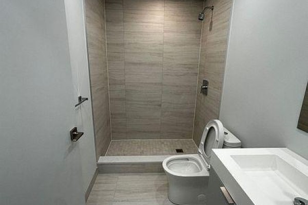 Another angle of the bathroom showcasing the walk-in shower, toilet, and vanity with a chrome faucet. - 1409 - 2920 Hwy 7, Vaughan